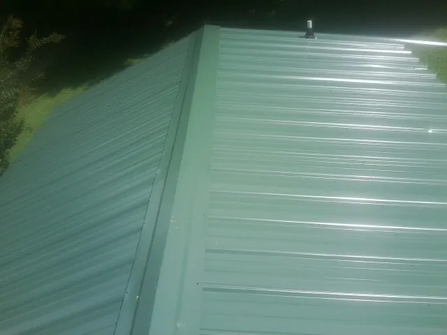 New green metal panels meeting at the ridge of a roof — Flat Roof Repair work by our crew in Newport News