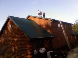 Crew on the ridge of a green metal roof on a two story log home in Newport News