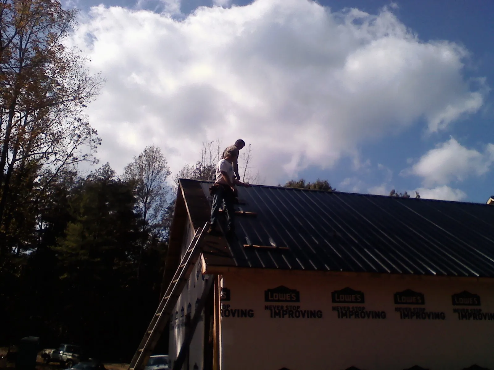 Roofer fastening dark metal panels high against a cloudy sky, from a Roof Inspection job in Newport News