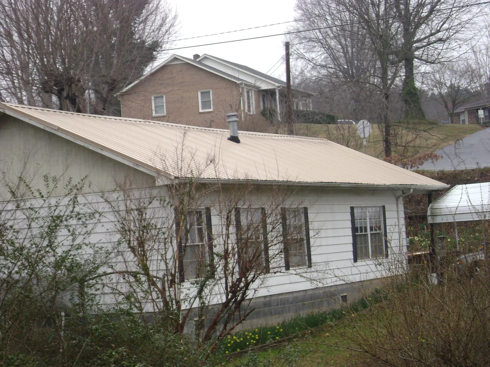 Tan metal roof on a white sided house set into a hillside — Commercial Roofing by Roofing Brothers in Newport News